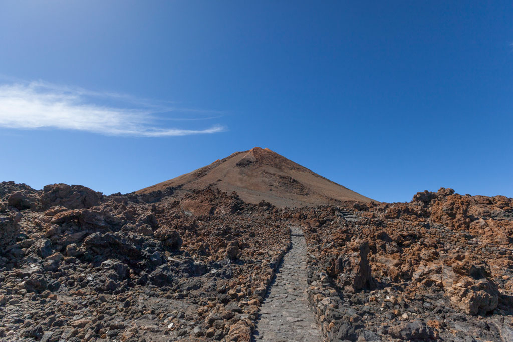 Een steenpad naar de berg Teide op Tenerife onder een blauwe lucht.