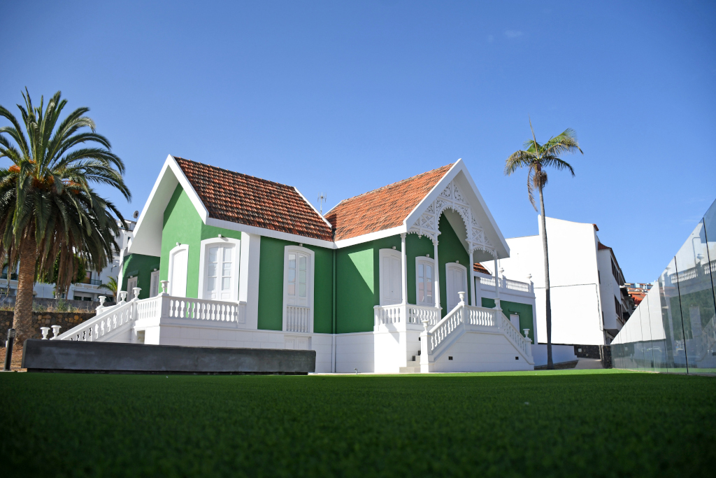 Oud groen en wit huis met rood dak op Tenerife, omringd door palmbomen en gazons.